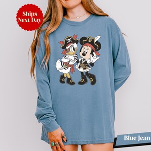 A woman wearing a blue long-sleeved shirt with a cartoon image of Minnie Mouse and Donald Duck dressed as pirates.