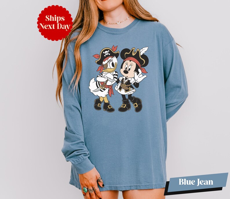 A woman wearing a blue long-sleeved shirt with a cartoon image of Minnie Mouse and Donald Duck dressed as pirates.