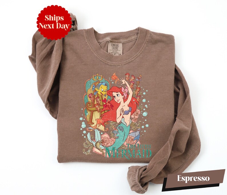 A brown t-shirt with a printed design of the mermaid character from the Disney animated film "The Little Mermaid".