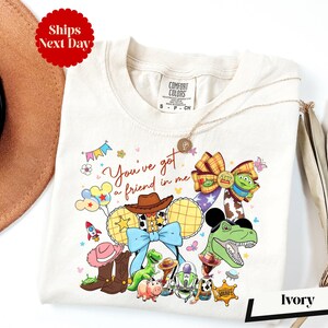 A white t-shirt with a colorful graphic design featuring characters from the Toy Story movie, including Woody, Buzz Lightyear, and other beloved characters.