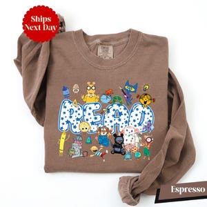 A brown t-shirt with a colorful graphic design featuring various cartoon characters and the word "READ" prominently displayed.