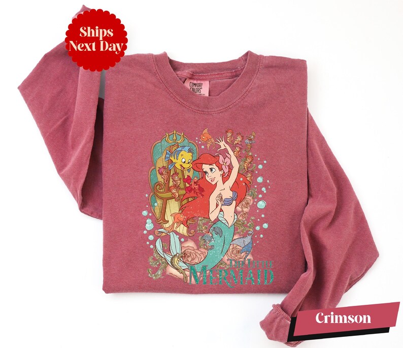 A pink long-sleeved shirt with a printed design featuring characters from the Disney animated film "The Little Mermaid".