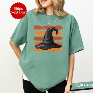 A woman wearing a green t-shirt with a graphic of a witch's hat printed on it.