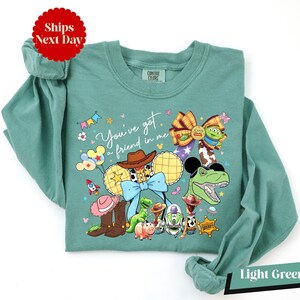 A green long-sleeved shirt with a colorful graphic design featuring various cartoon characters and a message.