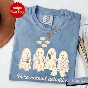 May include: A blue jean colored t-shirt featuring a graphic of five ghosts engaged in various tasks with speech bubbles saying d-a-t-a and the text Para normal activities printed below. The shirt has a crew neckline and a Comfort Colors brand label.