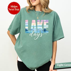 A woman wearing a green t-shirt with the word "LAKES" printed on it, standing against a white background.