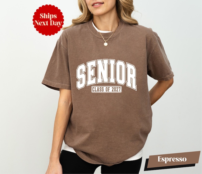 A woman wearing a brown t-shirt with the text "SENIOR CLASS OF 2027" printed on it.