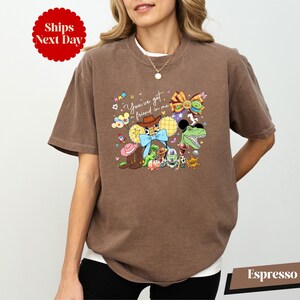 A woman wearing a brown t-shirt with a colorful graphic design featuring various cartoon characters and text.