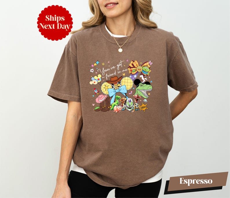 A woman wearing a brown t-shirt with a colorful graphic design featuring various cartoon characters and text.