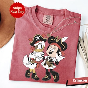 A red t-shirt with a cartoon image of Minnie Mouse and Donald Duck dressed as pirates, along with a necklace and a hat.