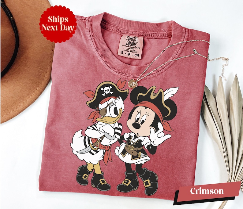 A red t-shirt with a cartoon image of Minnie Mouse and Donald Duck dressed as pirates, along with a necklace and a hat.