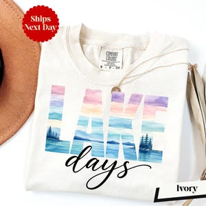 A white t-shirt with the word "LAKES" printed on it, along with a necklace and a hat, all placed on a white background.