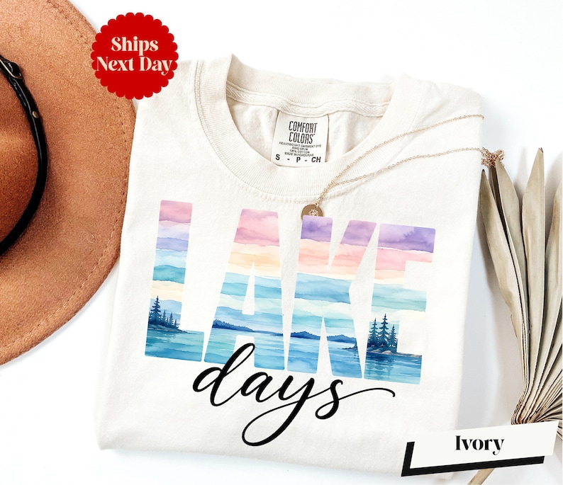 A white t-shirt with the word "LAKES" printed on it, along with a necklace and a hat, all placed on a white background.