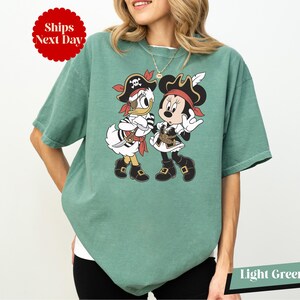A woman wearing a green t-shirt with a graphic of Minnie Mouse and Donald Duck in pirate costumes.