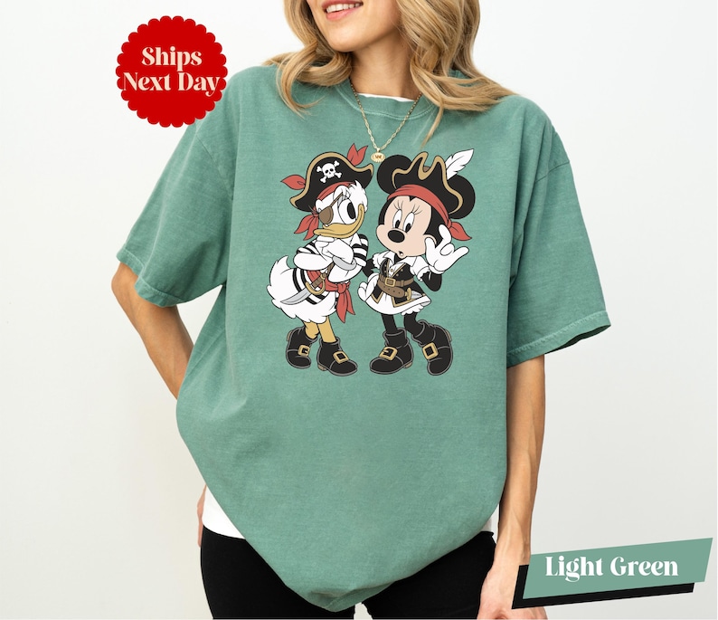 A woman wearing a green t-shirt with a graphic of Minnie Mouse and Donald Duck in pirate costumes.