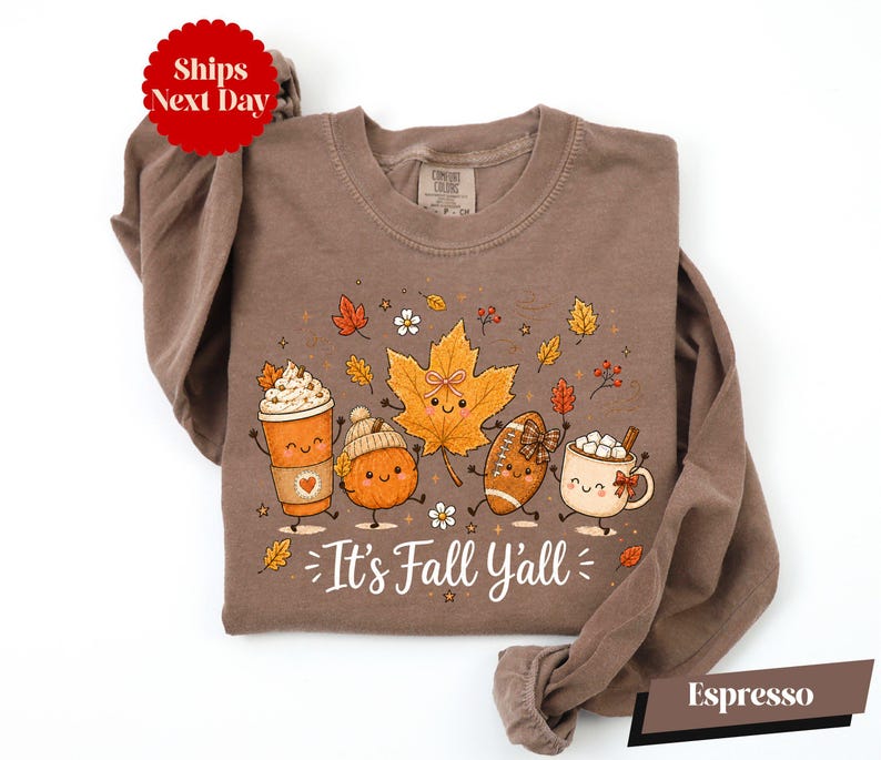 A brown long-sleeved t-shirt with a graphic design featuring cartoon characters and fall-themed elements such as leaves, pumpkins, and hot beverages.