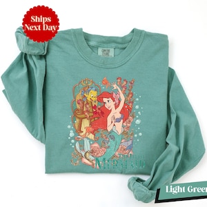 A light green t-shirt with a printed design of the mermaid character from the Disney animated film "The Little Mermaid".