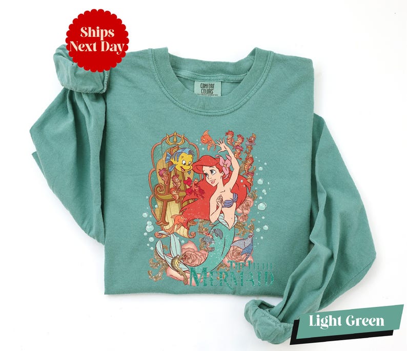 A light green t-shirt with a printed design of the mermaid character from the Disney animated film "The Little Mermaid".