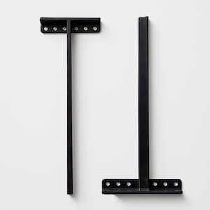 May include: Two black metal shelf brackets. Each bracket has a T-shape with a long vertical bar and a horizontal bar with pre-drilled holes for mounting. The brackets are designed for wall mounting and are made of a durable metal.