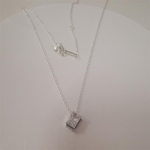 Peut inclure: Un collier en argent avec un pendentif carré en pierre précieuse transparente. Le pendentif est entouré d'un cadre carré plus petit et de couleur foncée. La chaîne est fine et argentée, avec un fermoir à l'arrière.