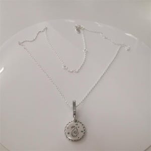 May include: A silver necklace with a pendant featuring a swan design. The pendant is round with a scalloped edge and small star accents. The chain is delicate and adjustable, suitable for various necklines.