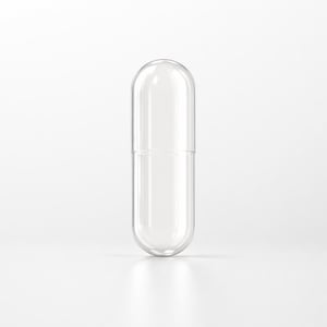 May include: A clear, empty capsule with a rounded top and bottom, designed to be filled. The capsule is made of transparent material, allowing a view of the interior. The capsule is standing upright on a white surface.