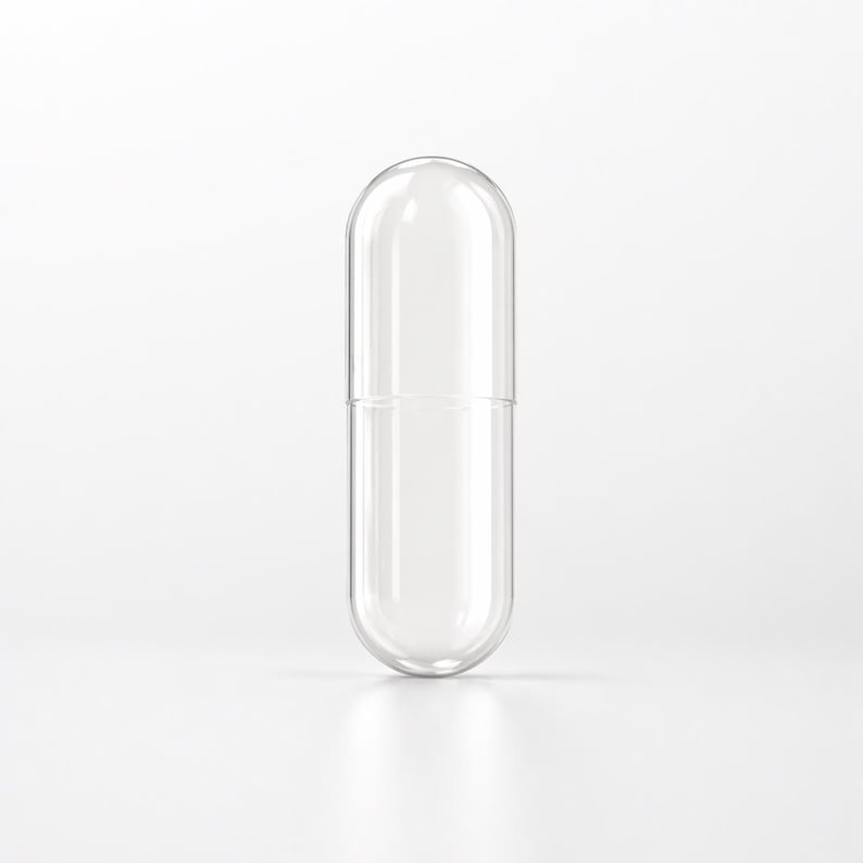 May include: A clear, empty capsule with a rounded top and bottom, designed to be filled. The capsule is made of transparent material, allowing a view of the interior. The capsule is standing upright on a white surface.