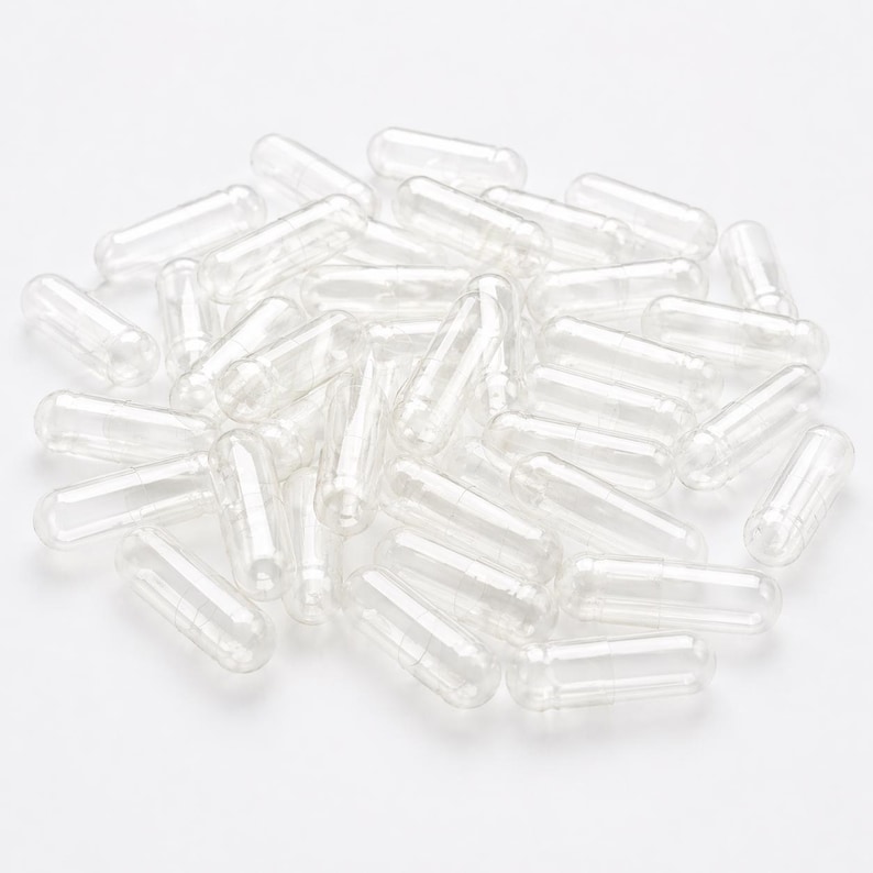 May include: A collection of clear, empty gelatin capsules, scattered on a white surface. The capsules are cylindrical with rounded ends, designed for filling with powders or supplements. The transparent material allows visibility of the contents.