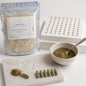 May include: A clear plastic bag filled with empty gelatin capsules, labeled "CapsuleCore GELATIN CAPSULES SIZE 00". A white capsule filling tray, a small bowl with a spoon, and filled capsules are also present. The image shows a set for making capsules.