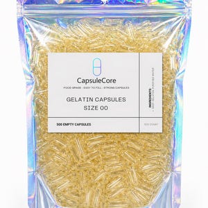 May include: A clear, holographic bag filled with numerous yellow gelatin capsules. The bag features a white label with the text "CapsuleCore," "Gelatin Capsules," and "Size 00." The label also indicates the contents are food grade and easy to fill. The bag contains 500 empty capsules.