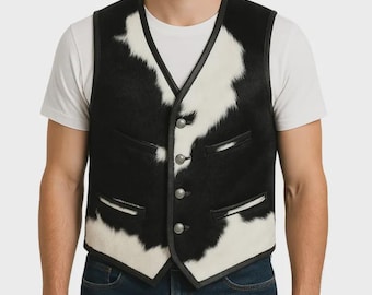 May include: A black and white cowhide vest with a V-neck and three silver buttons. The vest has black leather trim and two small pockets. The vest is worn over a white t-shirt and blue jeans.