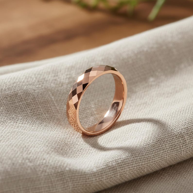 Peut inclure: Une bague en or rose avec un design &agrave; facettes. La bague est pos&eacute;e sur un tissu de couleur neutre, avec une ombre douce. La surface de la bague refl&egrave;te la lumi&egrave;re, soulignant son motif g&eacute;om&eacute;trique. C'est un bijou.