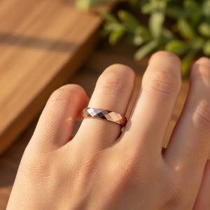 Peut inclure: Une bague en or rose avec un design g&eacute;om&eacute;trique &agrave; facettes. La bague est port&eacute;e au doigt, mettant en valeur sa surface polie et le jeu de la lumi&egrave;re sur ses facettes. Le design de la bague pr&eacute;sente une s&eacute;rie de plans inclin&eacute;s, cr&eacute;ant un effet scintillant.