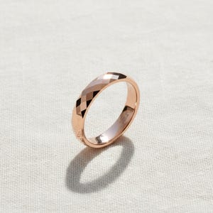 Peut inclure: Bague en or rose avec un design &agrave; facettes. La bague pr&eacute;sente un motif g&eacute;om&eacute;trique de surfaces angulaires. La bague est pos&eacute;e sur un fond blanc.