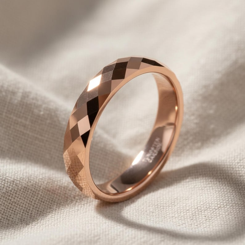 Peut inclure: Bague en or rose avec un design &agrave; facettes. La bague pr&eacute;sente un motif g&eacute;om&eacute;trique de losanges autour de l'anneau. La bague est pr&eacute;sent&eacute;e sur un fond en tissu de couleur neutre.