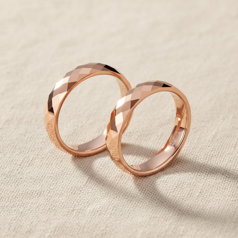 Peut inclure: Deux bagues en or rose avec un design &agrave; facettes. Les bagues sont pr&eacute;sent&eacute;es sur une surface de couleur neutre. Les bagues ont un motif g&eacute;om&eacute;trique, captant la lumi&egrave;re et cr&eacute;ant un effet scintillant. Les bagues sont probablement pour un mariage ou des fian&ccedil;ailles.
