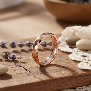 Peut inclure: Bague en or rose avec un design &agrave; facettes. La bague est pr&eacute;sent&eacute;e sur une surface en bois avec des brins de lavande et de petites pierres. La surface de la bague refl&egrave;te la lumi&egrave;re. C'est une bague de type alliance.