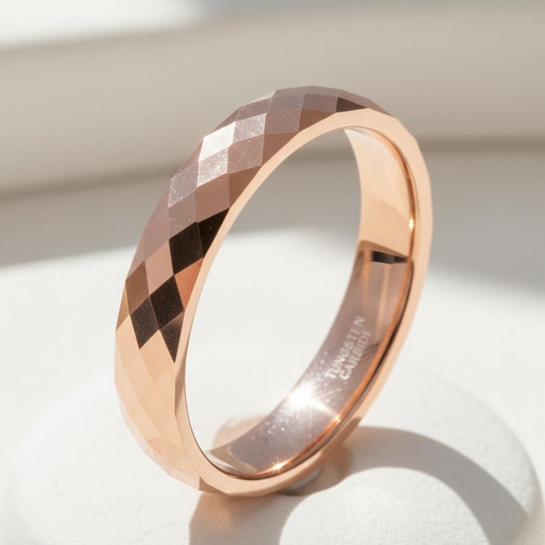 Peut inclure: Bague en carbure de tungst&egrave;ne or rose avec un design g&eacute;om&eacute;trique &agrave; facettes. La surface de la bague refl&egrave;te la lumi&egrave;re, mettant en valeur ses multiples facettes. L'int&eacute;rieur de la bague porte l'inscription "Tungsten Carbide".