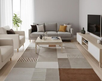 May include: A modern living room featuring a gray sofa with accent pillows, two cream-colored armchairs, and a light wood coffee table. A large area rug with geometric patterns in shades of brown, beige, and gray covers the floor. A TV and white cabinet complete the room.