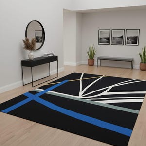 May include: A black rectangular area rug with a geometric design. The rug features a bold blue stripe, white lines, and accents of yellow and gray. The rug is placed on a light wood floor in a room with neutral walls.