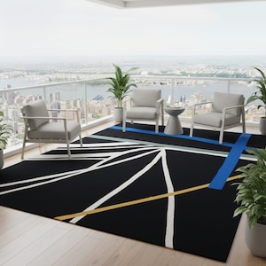 May include: Black outdoor rug with a geometric design featuring white, yellow, and blue lines. The rug is placed on a wooden deck, with two gray chairs and a small table. Potted plants and a city skyline are visible in the background.