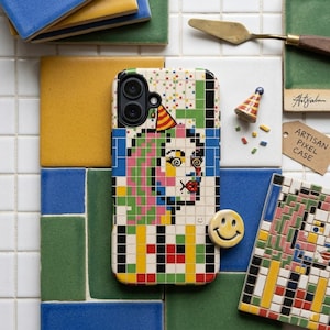 May include: A colorful pixel art phone case featuring a face with a party hat, surrounded by colorful tiles. The case is labeled "ARTISAN PIXEL CASE" on a tag. A yellow smiley face and a miniature party hat are also present.