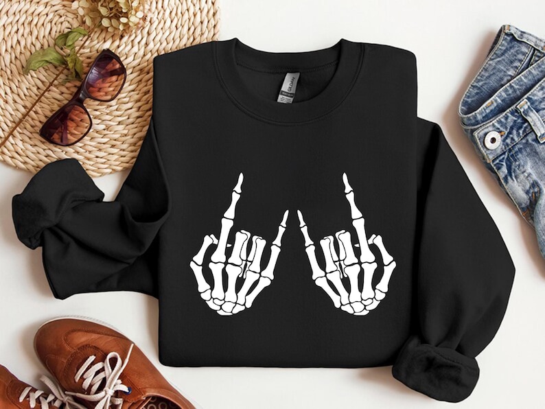 May include: A black long-sleeve crewneck sweatshirt featuring a white graphic print of two skeleton hands positioned to display the rock and roll hand sign. The sweatshirt has a ribbed collar, cuffs, and hem, with a standard fit and solid black fabric.