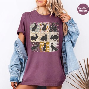 Puede incluir: Camiseta color borgo&ntilde;a con un dise&ntilde;o de patchwork con nueve cuadrados. Cada cuadrado muestra una silueta de conejo negro sobre un fondo floral o estampado. La camiseta se lleva con una chaqueta vaquera.