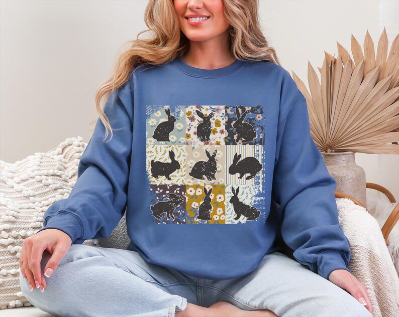 Puede incluir: Una sudadera azul con un dise&ntilde;o de patchwork. Presenta siluetas de conejos negros sobre cuadrados florales y estampados. La sudadera tiene cuello redondo y mangas largas.