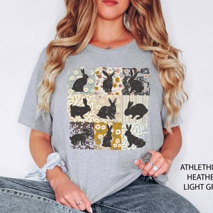 Puede incluir: Camiseta gris claro con un dise&ntilde;o de retazos de siluetas de conejos negros sobre cuadrados florales y estampados. La camiseta tiene cuello redondo y mangas cortas. El texto "ATHLETHICH HEATHER LIGHT GREY" est&aacute; impreso en el lado derecho.
