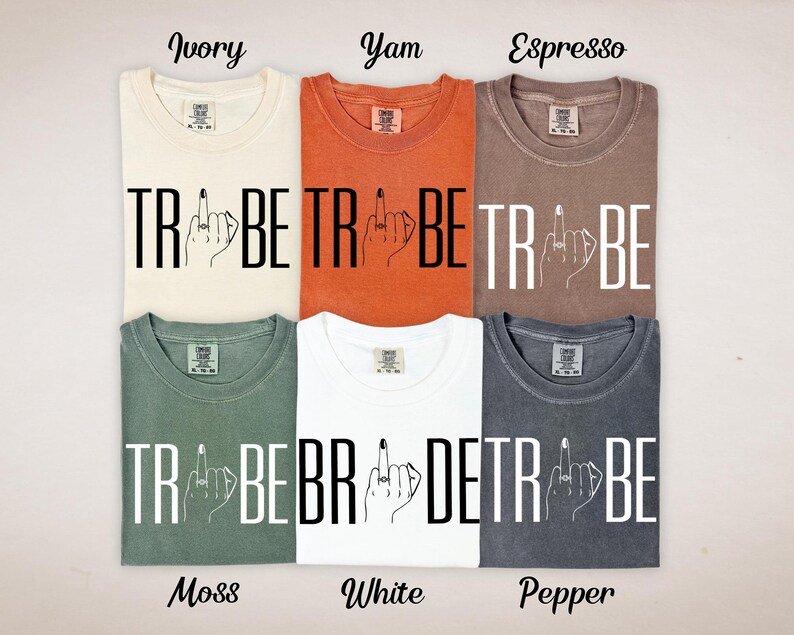 May include: Six different colored t-shirts, including ivory, yam, espresso, moss, white, and pepper. Each shirt has the word "TRIBE" printed in large, bold, white letters, with a hand graphic giving the middle finger.