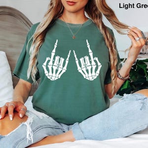 May include: A light green t-shirt featuring a white graphic of two skeleton hands making the rock and roll hand gesture. The shirt has a crew neckline and short sleeves. The text Light Green is printed in the upper right corner of the image.