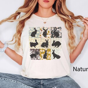 Puede incluir: Camiseta color crema con una cuadr&iacute;cula de nueve cuadrados, cada uno con una silueta de conejo negro sobre un fondo floral o estampado. La palabra "Natural" est&aacute; impresa en negro en la parte inferior derecha.