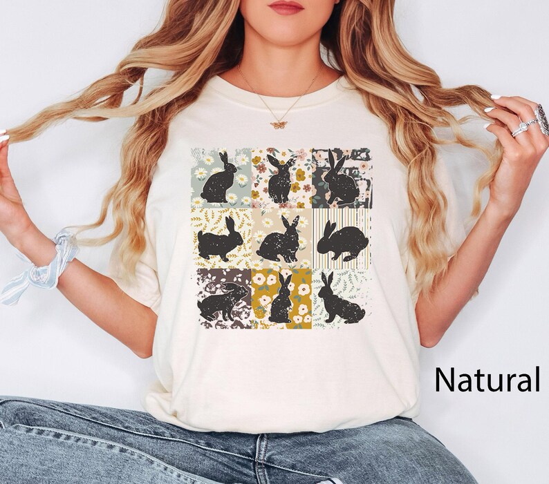 Puede incluir: Camiseta color crema con una cuadr&iacute;cula de nueve cuadrados, cada uno con una silueta de conejo negro sobre un fondo floral o estampado. La palabra "Natural" est&aacute; impresa en negro en la parte inferior derecha.